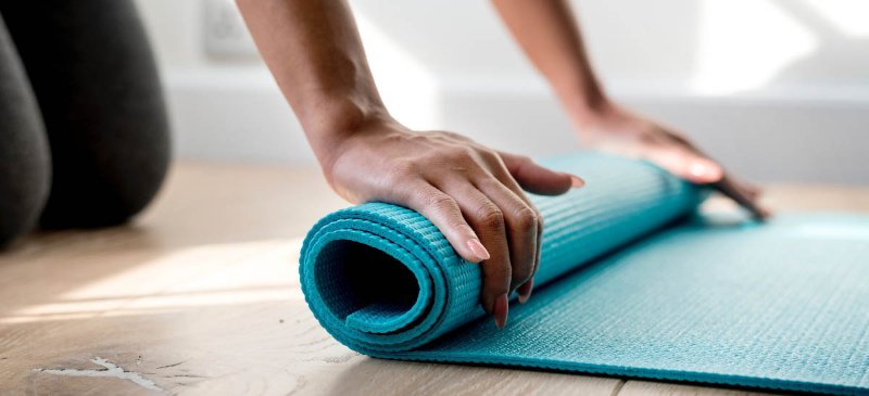 Shot of a Woman rolling yoga mat on the floor after a class