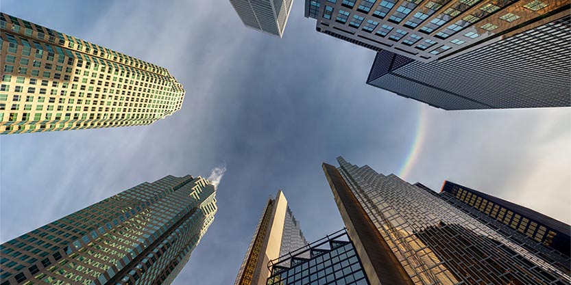 Looking up at a rainbow halo in the blue sky with tall city buildings