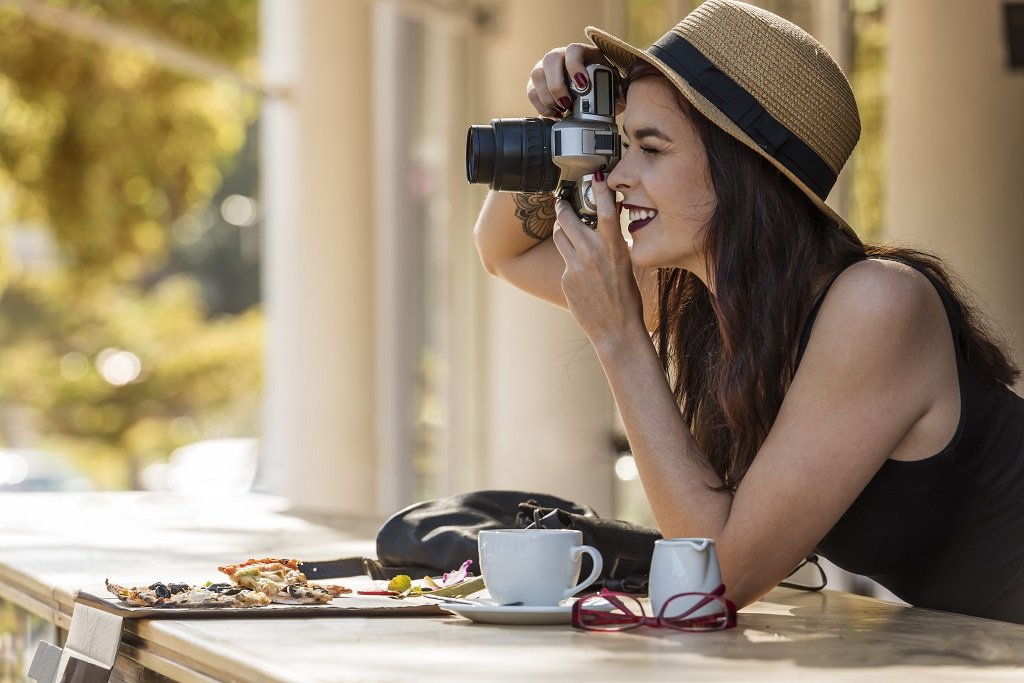 young beautiful traveler happily taking photos with camera at cafe