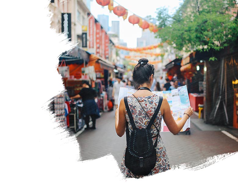 Rear view image of a young brunette woman. She is enjoying the walk and exploring the city, wearing a casual but fashionable dress, sightseeing and shopping on the Singapore street market. She is holding a large city map, checking out where to go next.