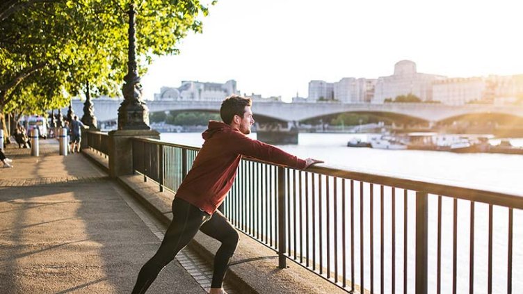 Young sporty man with earphones stretching on a railing