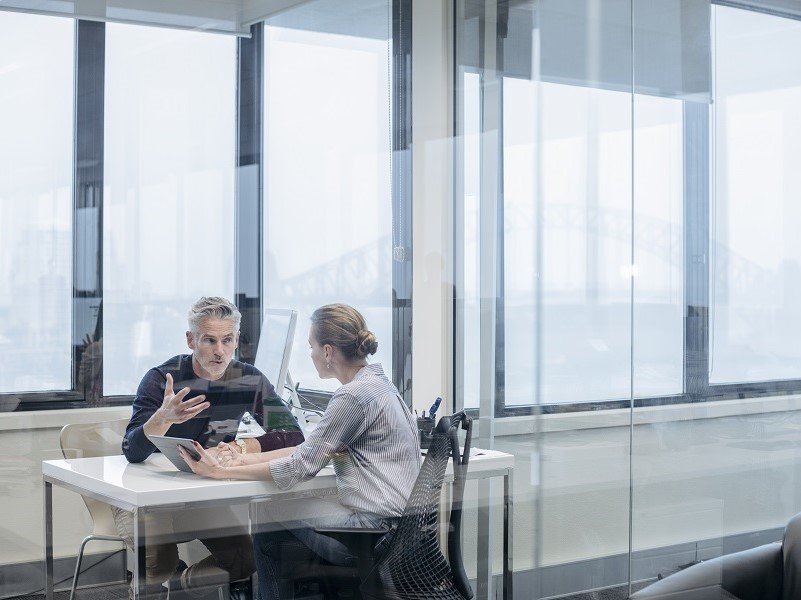 one male and female employee sitting in office cabing and discussing