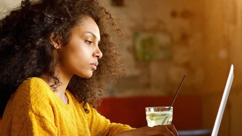 A woman sitting and working on her laptop(a glass of juice is placed on table)