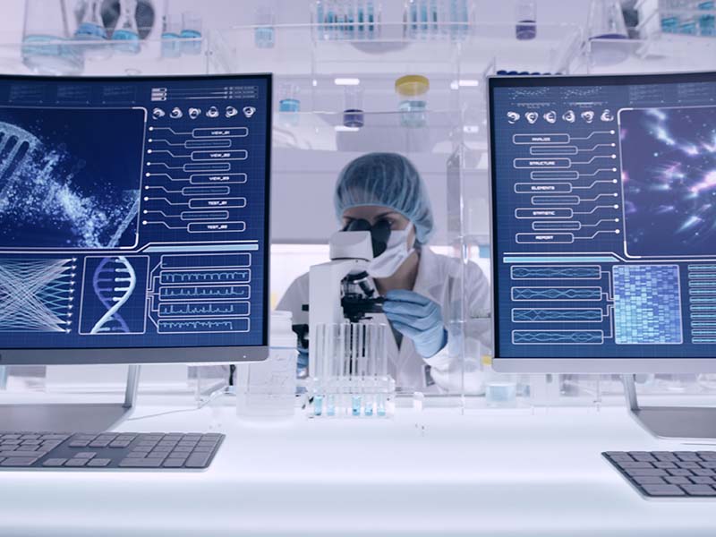 Life sciences laboratory with a scientist at work between two computer screens showing scientific data.