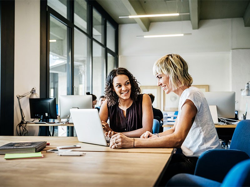 Two woman smiling while working on laptop	