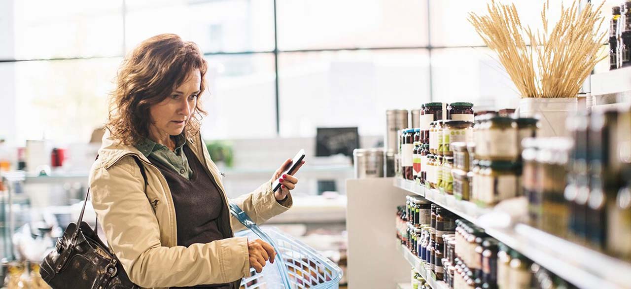 Woman holding smartphone while shopping in the supermarket